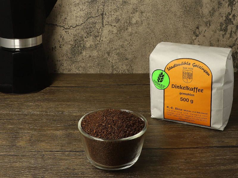 Gemahlener Dinkelkaffee in einem Glassch&auml;lchen auf einem Holztisch, dahinter die 500-g-T&uuml;te der Stadtm&uuml;hle Geisingen