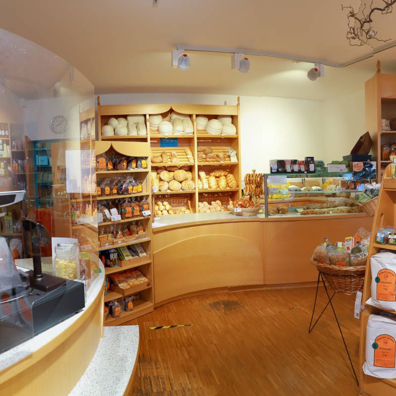 Blick in den Mühlenladen Geisingen: helle Holzregale mit Broten und Weckle, davor eine geschwungene Theke mit Kasse und eine Kühlvitrine