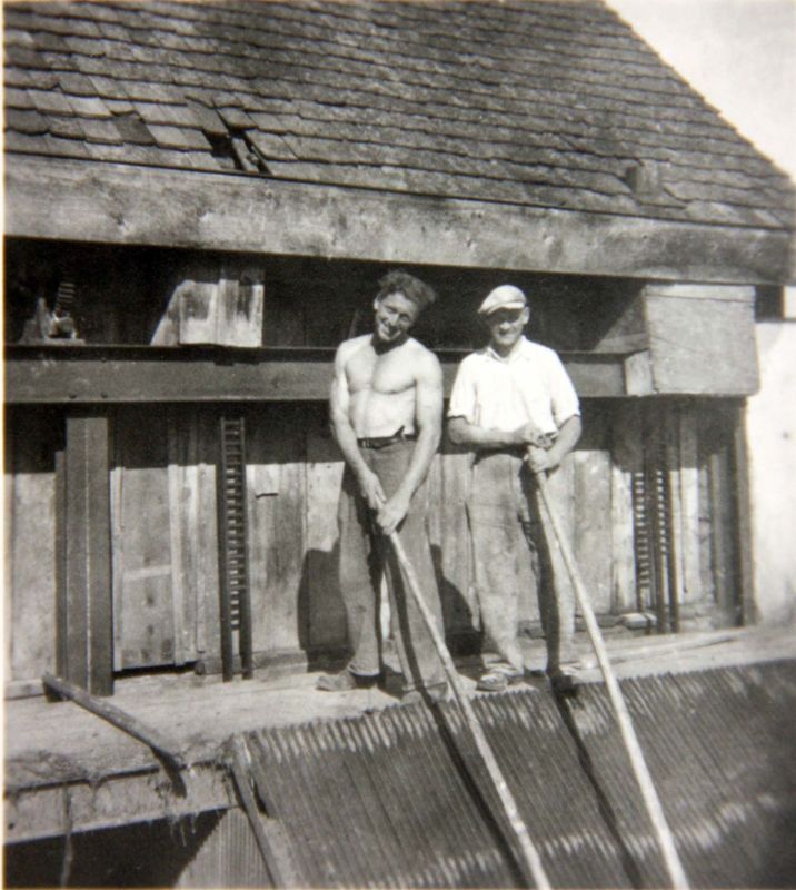 Two men with long-handled hooks at the trash rack of the mill race
