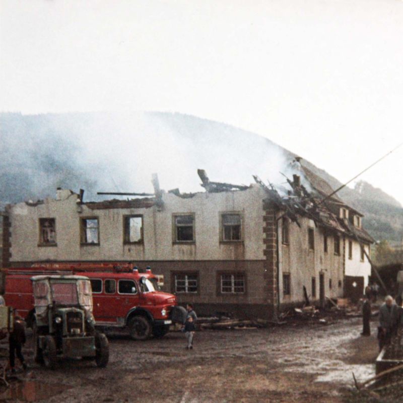 The burnt-out mill building without its roof, a fire engine and onlookers in front