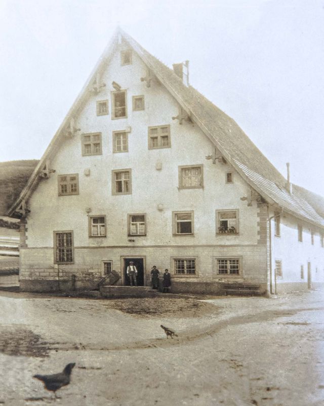 The old mill building with its tall gable, three people in the gateway, hens in the yard
