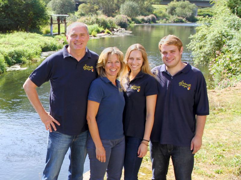 Four people in polo shirts with the mill crest on the riverbank