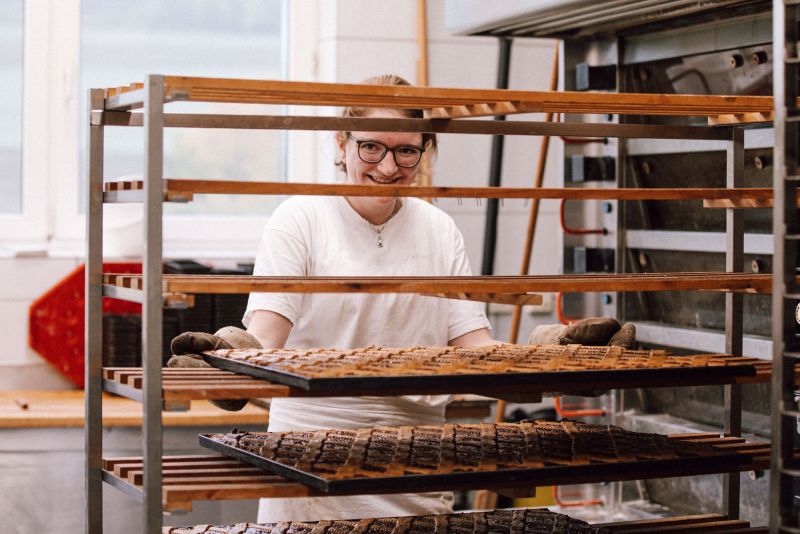 A baker behind a rack of full baking trays